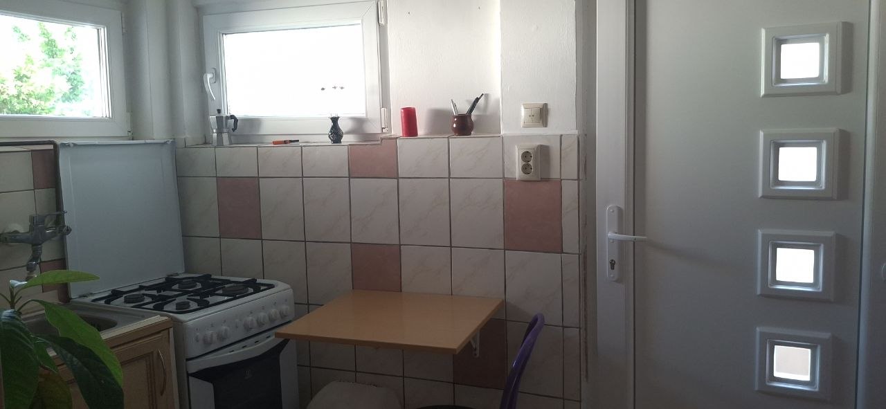 Konyhasarok gáztűzhellyel és kis asztallal az ablak mellett